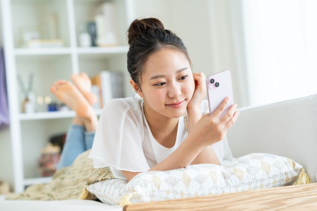 うつ伏せで寝転がってスマホを操作している女性