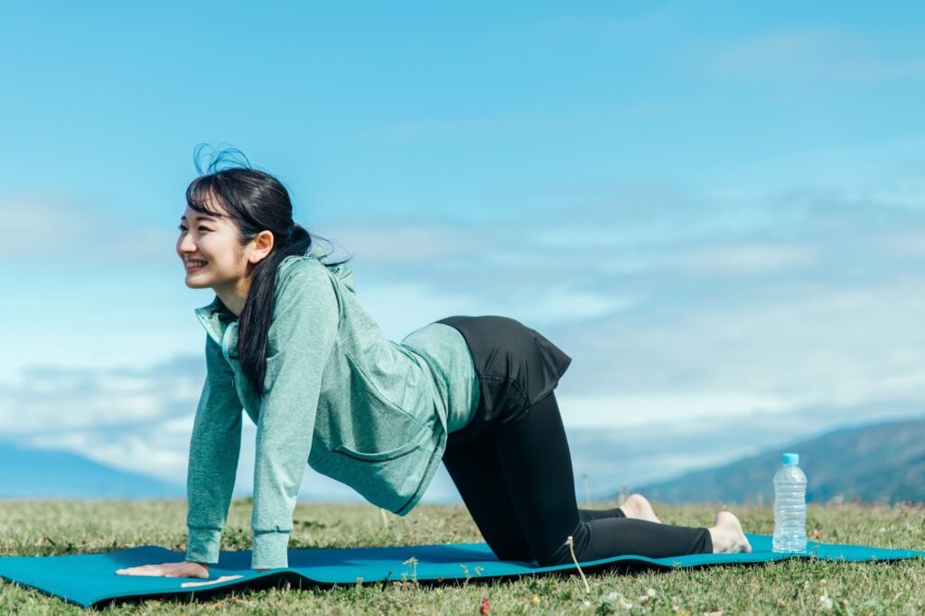 青空の下で反り腰による腰痛対策のストレッチをしている女性