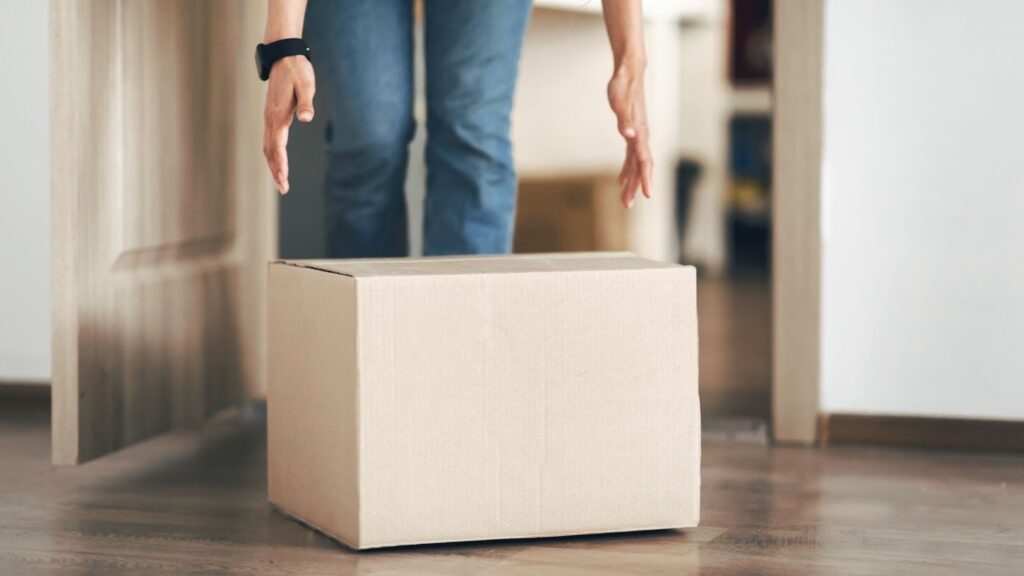 床に置かれた段ボール箱を持ち上げようとする人
