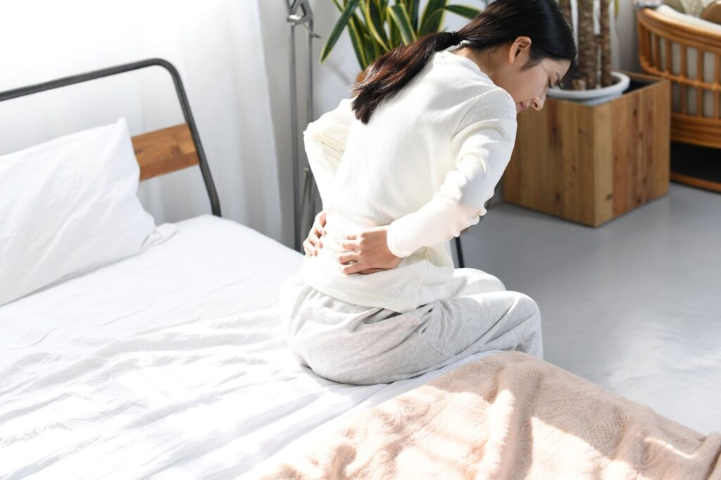 ぎっくり腰でつらそうにベッドに腰掛ける女性