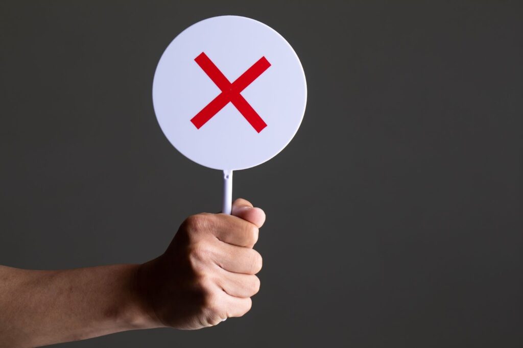 バツマークが書かれたパドルサインを持つ手元