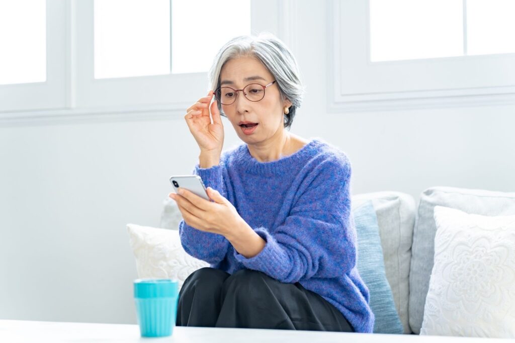 ソファに座ってスマホを見るメガネの更年期女性