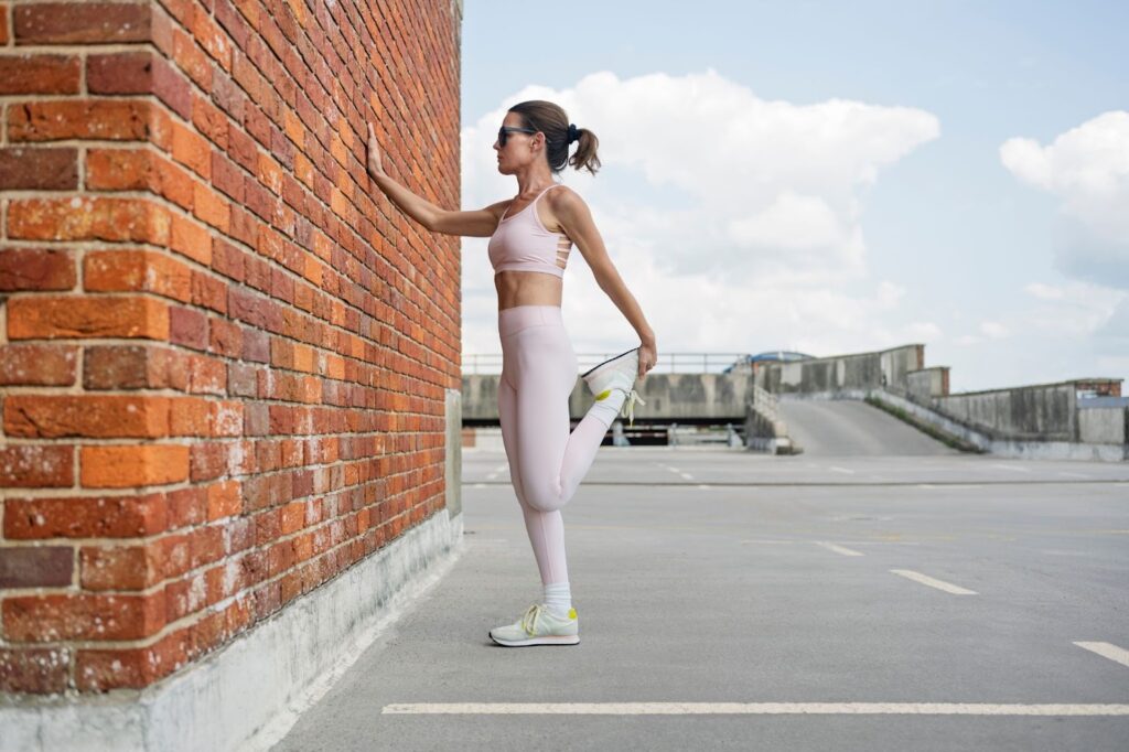 壁に手をついて膝痛の筋肉をほぐすストレッチをしている女性